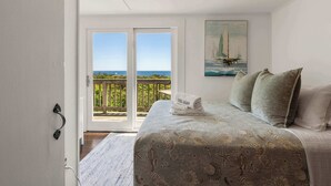 Une chambre à coucher avec un lit, un tableau représentant un voilier et un balcon avec vue sur la mer.