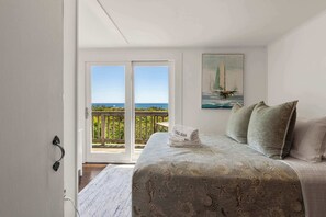 A bedroom with a bed, a painting of a sailboat, and a balcony with a view of the sea.