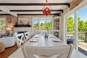A dining area with a white table set for four, a fireplace, and a view of the outdoors. - Walk to Oceanside Beach! (Wellfleet)