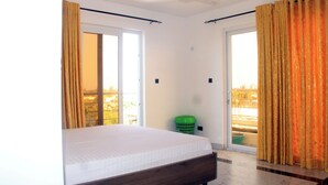 Ein Schlafzimmer mit einem Bett, einem grünen Wäschekorb und Blick durch das Fenster.