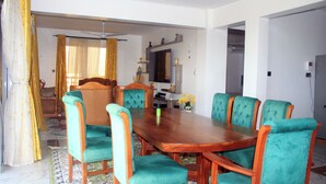 Ein Esszimmer mit einem Holztisch, stuhlähnlichen Sitzgelegenheiten in Türkisgrün, einem Deckenventilator und einem großen Spiegel über dem Tisch.