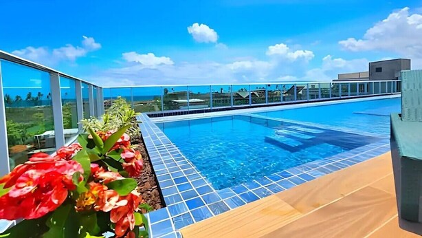 A rooftop infinity pool with clear blue water, surrounded by glass railings and a wooden deck.
