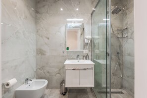 A modern bathroom with a bidet, a glass-enclosed shower, and a vanity with a mirror. - Adriatic Seaview 1 by PS (kavaje)