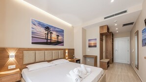 A modern hotel room with a large bed, a nightstand, a wooden headboard, a wall-mounted shelf, and a door leading to a closet. - Adriatic Seaview 1 by PS (kavaje)