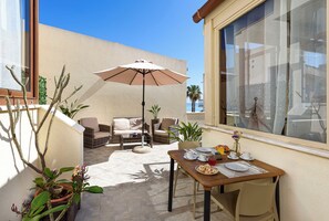 Eine sonnendurchflutete Terrasse mit Frühstückstisch, Gartenmöbeln und Blumentöpfen.