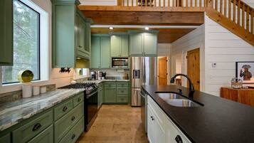 A kitchen with green cabinets, a stainless steel refrigerator, a black countertop, and a wooden staircase.