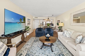 A living room with a large TV, two blue armchairs, a beige sofa, and a coffee table. - South Hampton 1003 Renovated w/Pool Beach (Myrtle Beach)