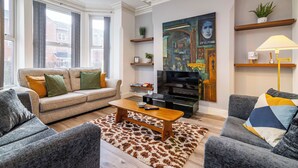 Ein modernes Wohnzimmer mit einer Couch, Sesseln, einem Couchtisch, einem Fernseher und einem Bild an der Wand.