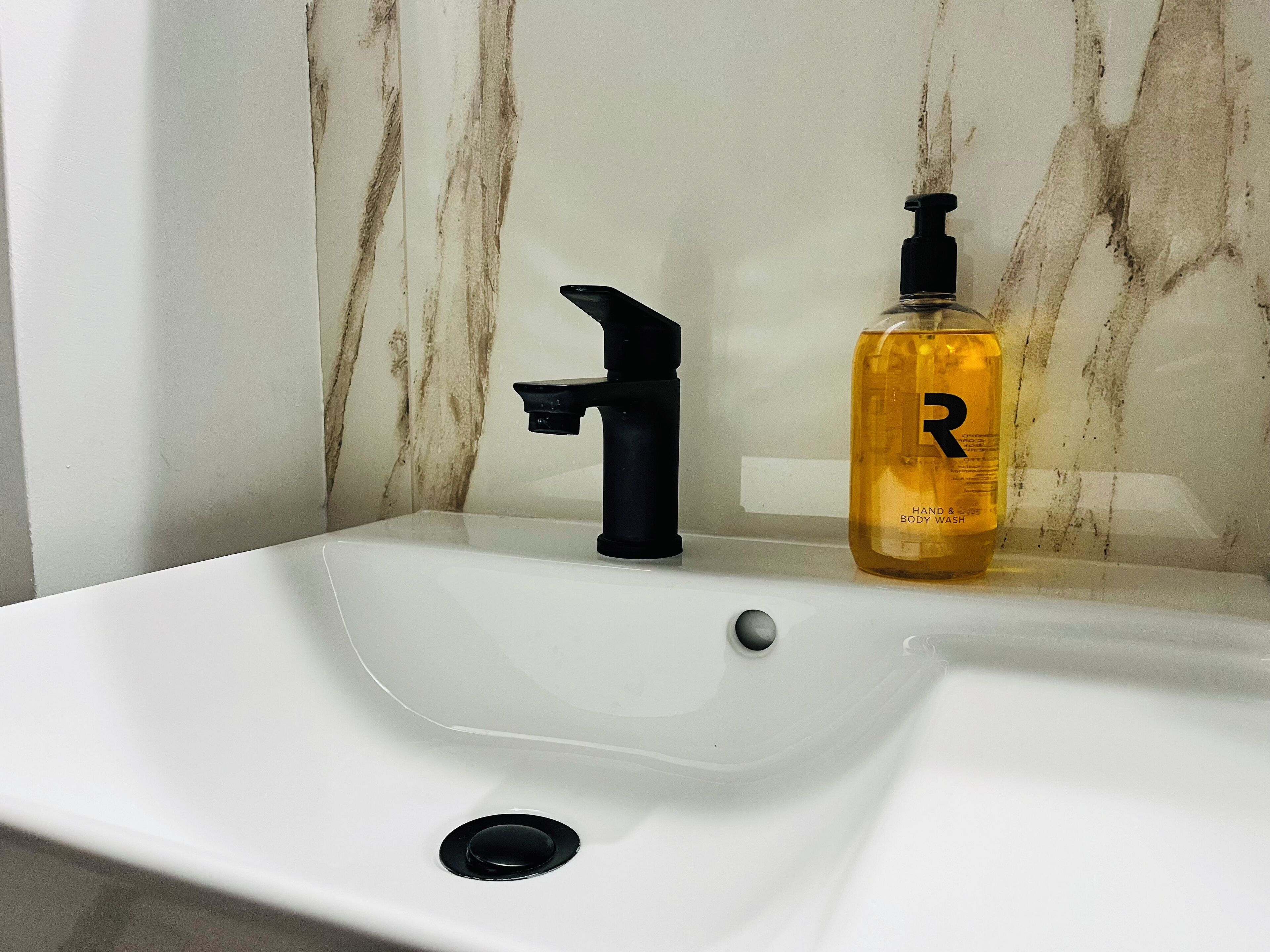 Un lavabo de salle de bain avec un robinet noir et une bouteille de savon pour les mains et le corps.