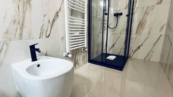 Une salle de bain moderne équipée d’un bidet, d’une douche à parois de verre et d’un mur recouvert de carreaux blancs.