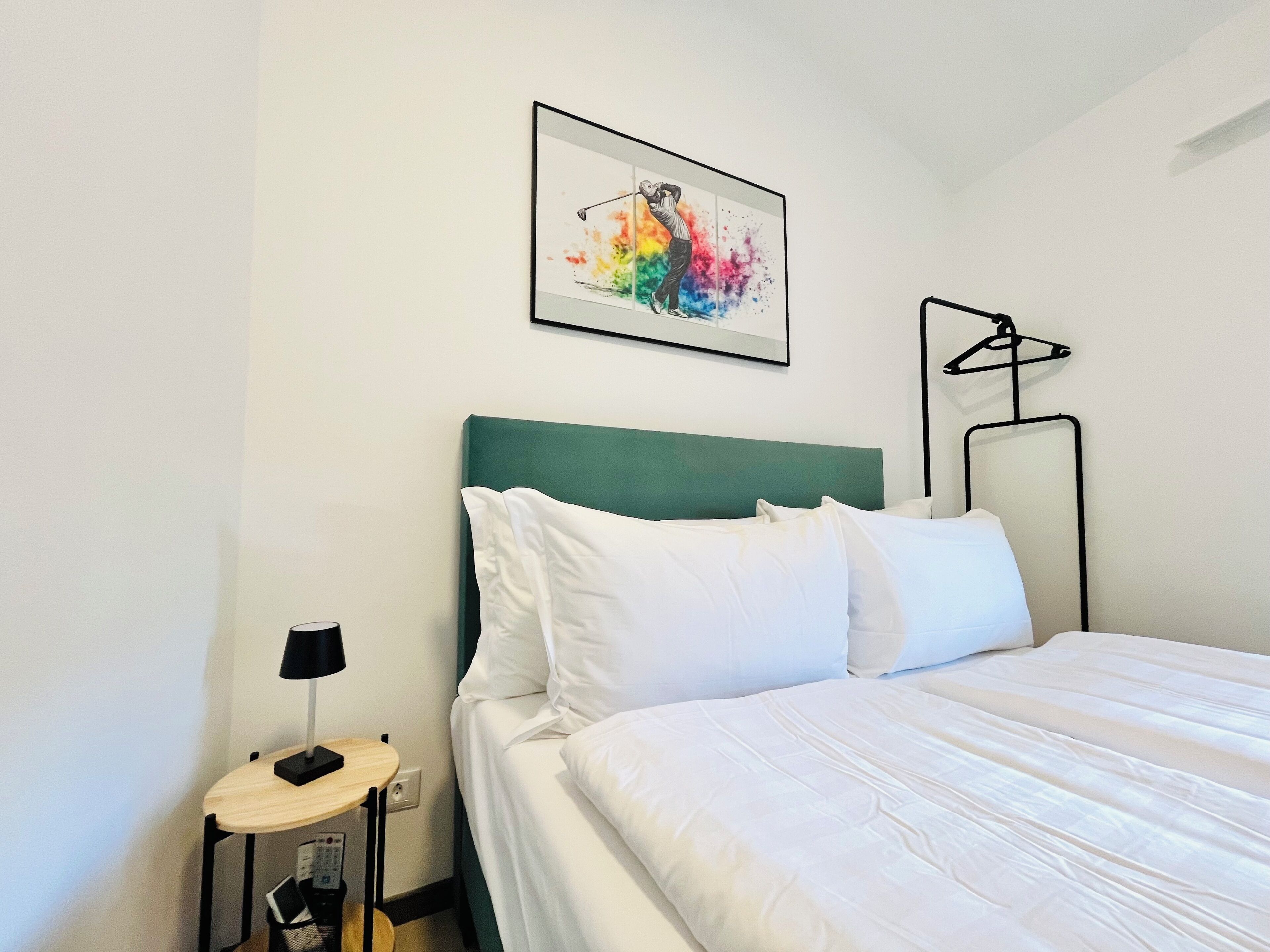 A neatly made bed with white bedding, a green headboard, and a framed artwork above it.