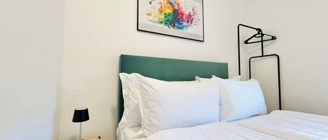 A neatly made bed with white bedding, a green headboard, and a framed artwork above it.