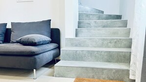 Un salon moderne avec un canapé gris, un escalier et un paillasson.
