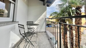 Un balcon avec une table et des chaises, une fenêtre et une vue sur des palmiers et des immeubles.