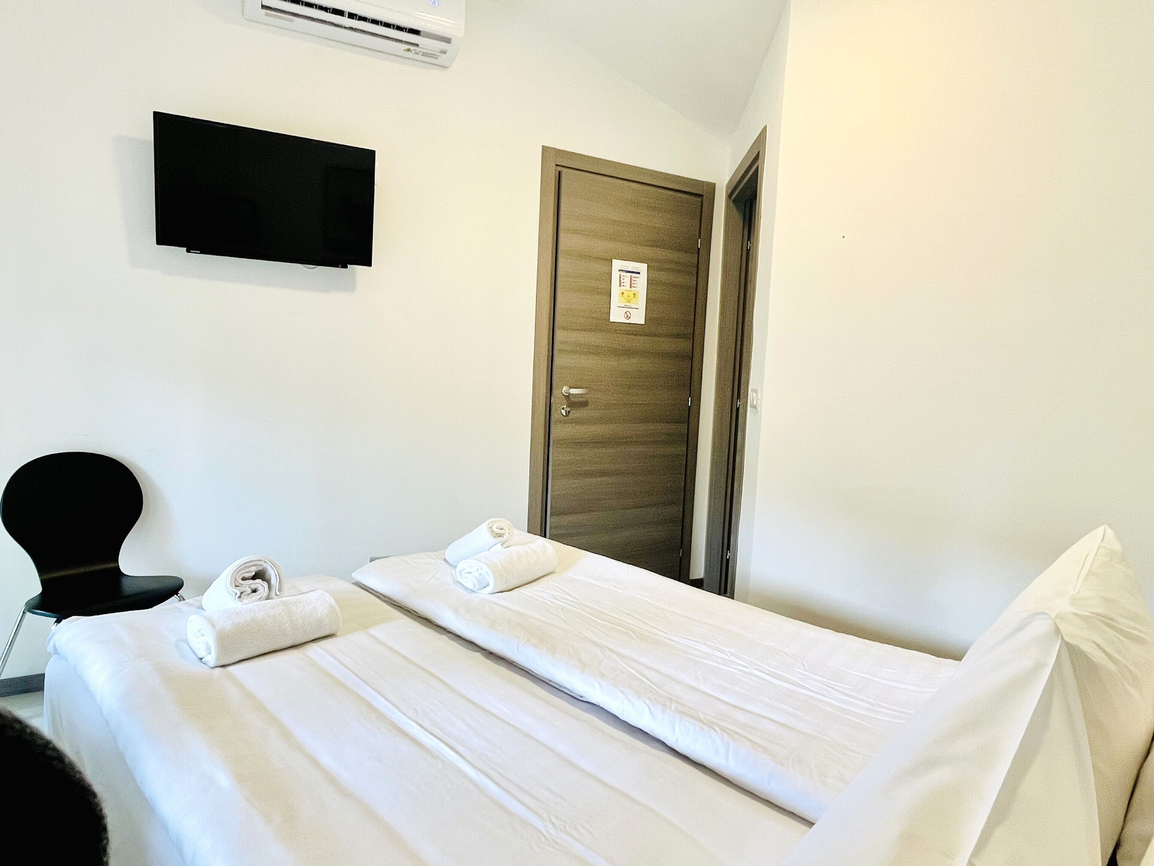 Une chambre d’hôtel avec un lit, un téléviseur à écran plat fixé au mur et une porte en bois.
