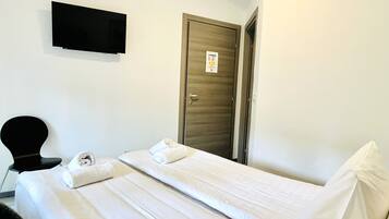 Una camera d'albergo con un letto, una TV a schermo piatto fissata al muro e una porta in legno.