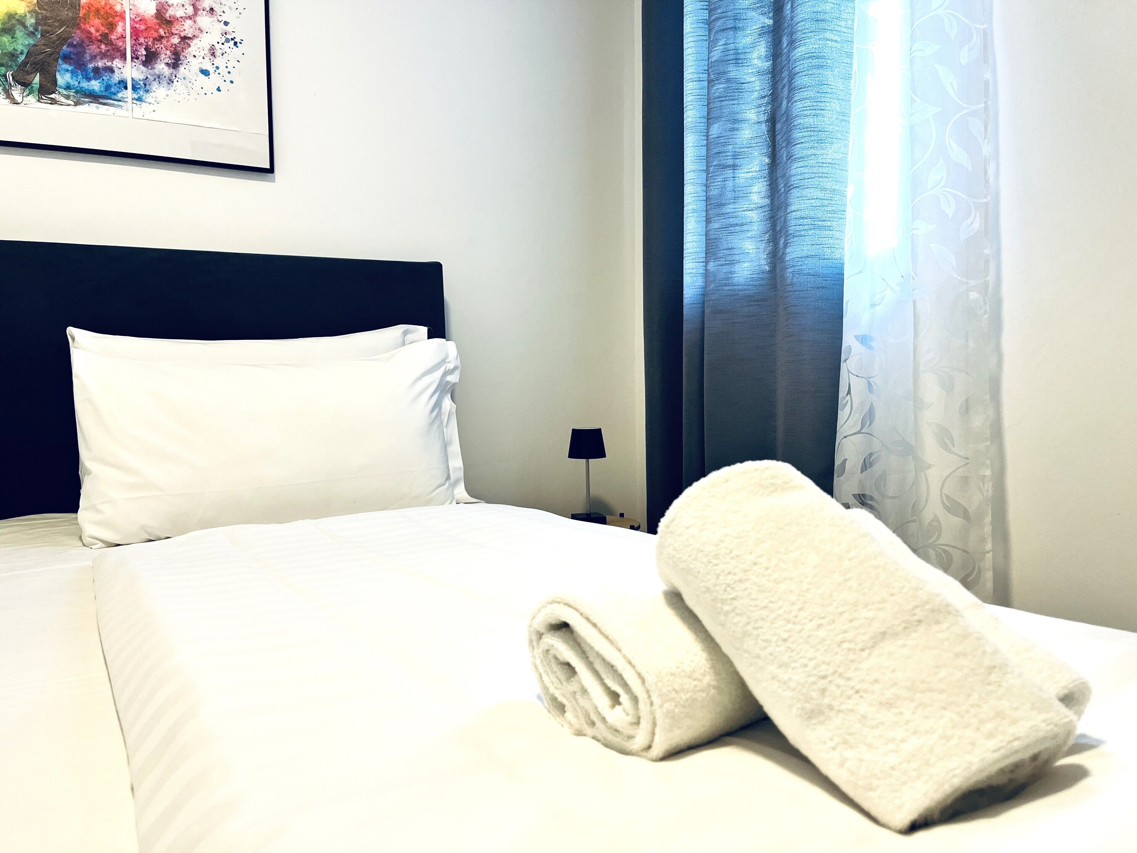 A neatly made bed with white linens, a rolled white towel, and a dark blue headboard.