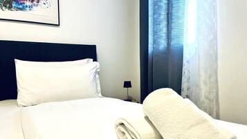 A neatly made bed with white linens, a rolled white towel, and a dark blue headboard.