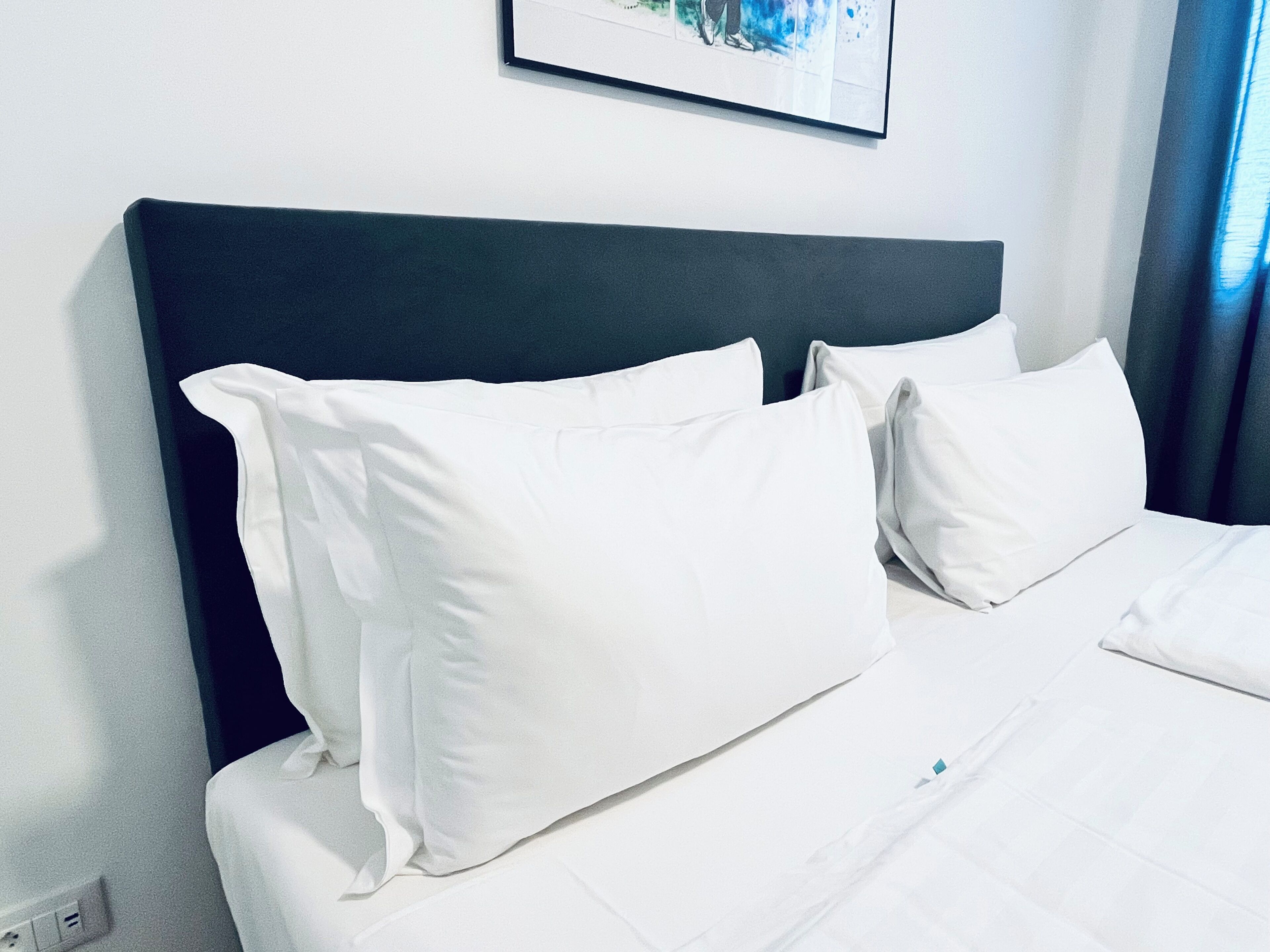 A neatly made bed with white linens and pillows, a dark headboard, and a framed picture on the wall.