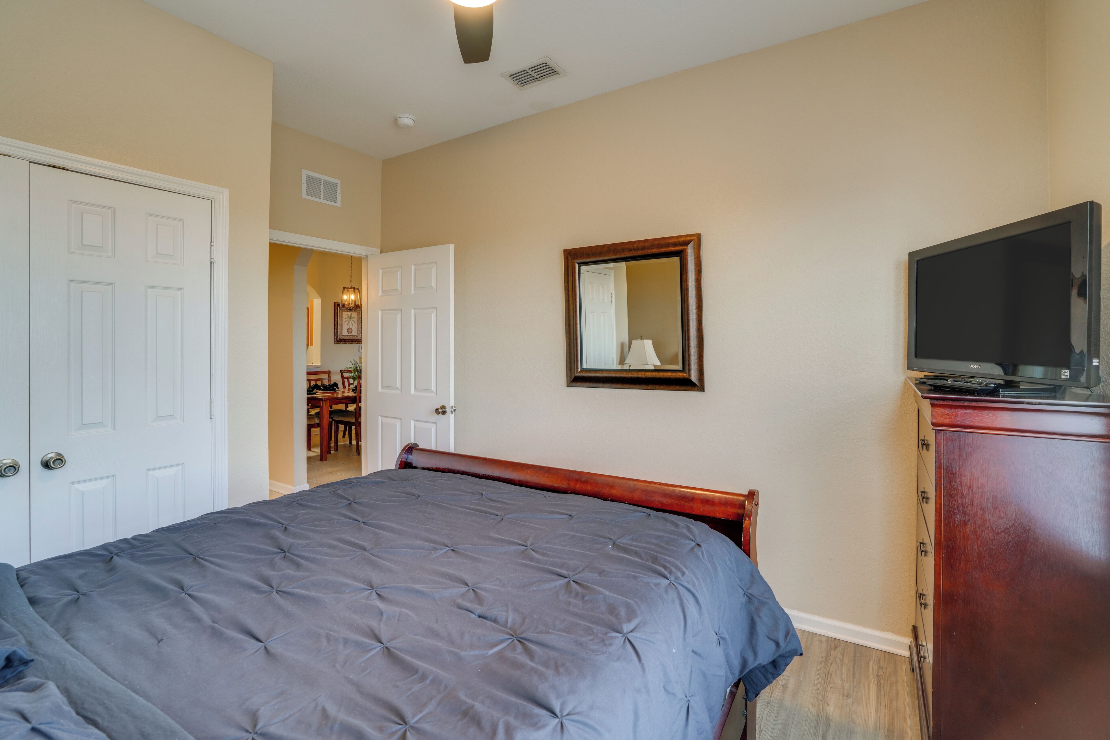 A bedroom with a bed, a dresser, a TV, and a door leading to another room.