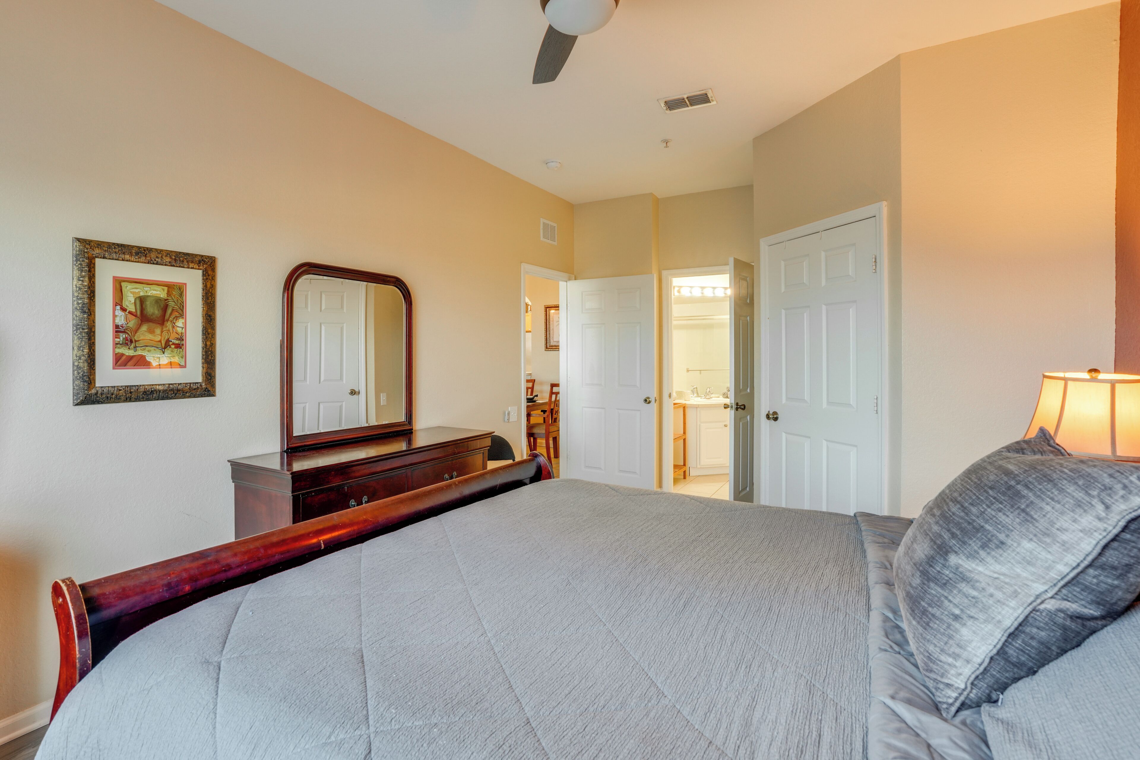 A bedroom with a bed, dresser, mirror, and a door leading to another room.