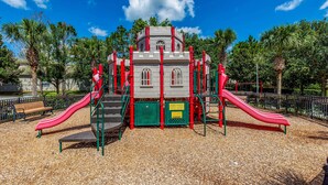Ein Spielplatz mit zwei roten Rutschen, einer Kletterkonstruktion und einer Bank.