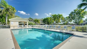 A swimming pool with lounge chairs and palm trees, surrounded by a fence. - 5 Mi to Jetblue Park: Condo w/ Pool & Pickleball (Fort Myers)
