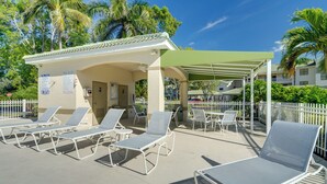 A poolside area with lounge chairs, a covered seating area, and a building with a sign indicating pool rules. - 5 Mi to Jetblue Park: Condo w/ Pool & Pickleball (Fort Myers)