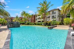 A swimming pool with clear blue water, surrounded by palm trees and a building with balconies. - Palm View- 9 Pools BBQ Gym (Westcourt)