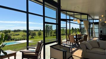 A spacious living area with large windows, a pool, and outdoor furniture.
