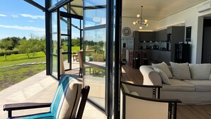 A modern interior with large glass windows, a dining area, a kitchen, and a living room with a sofa. - Panoramic by Carmelodays (Carmelo)