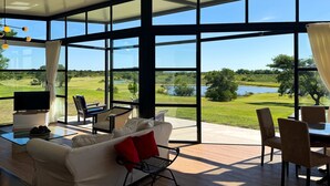 A modern living room with a large glass wall offering a scenic view of a golf course and lake. - Panoramic by Carmelodays (Carmelo)