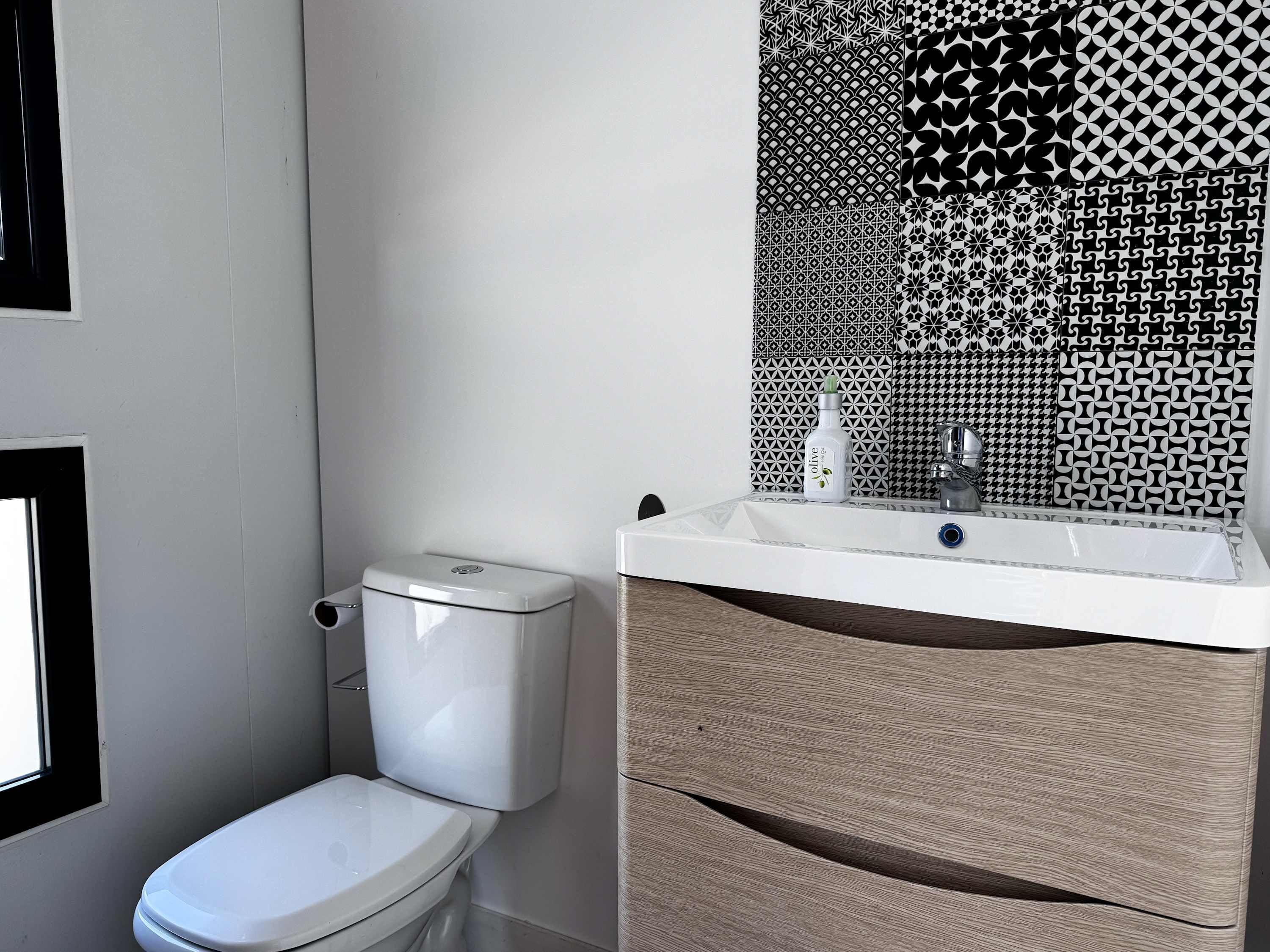 Un baño con inodoro blanco, lavamanos con espejo y un salpicadero con diseño.