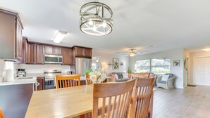 Cozinha espaçosa com armários de madeira, mesa de jantar e cadeiras. Há uma janela grande que oferece luz natural e vista para o exterior.