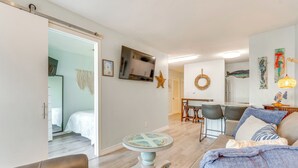 A modern living room with a sofa, a coffee table, and a TV mounted on the wall. There is a dining area with a table and chairs, and a kitchen in the background. - Walk to Beach: Resort Retreat w/ Balcony in Destin (Destin)
