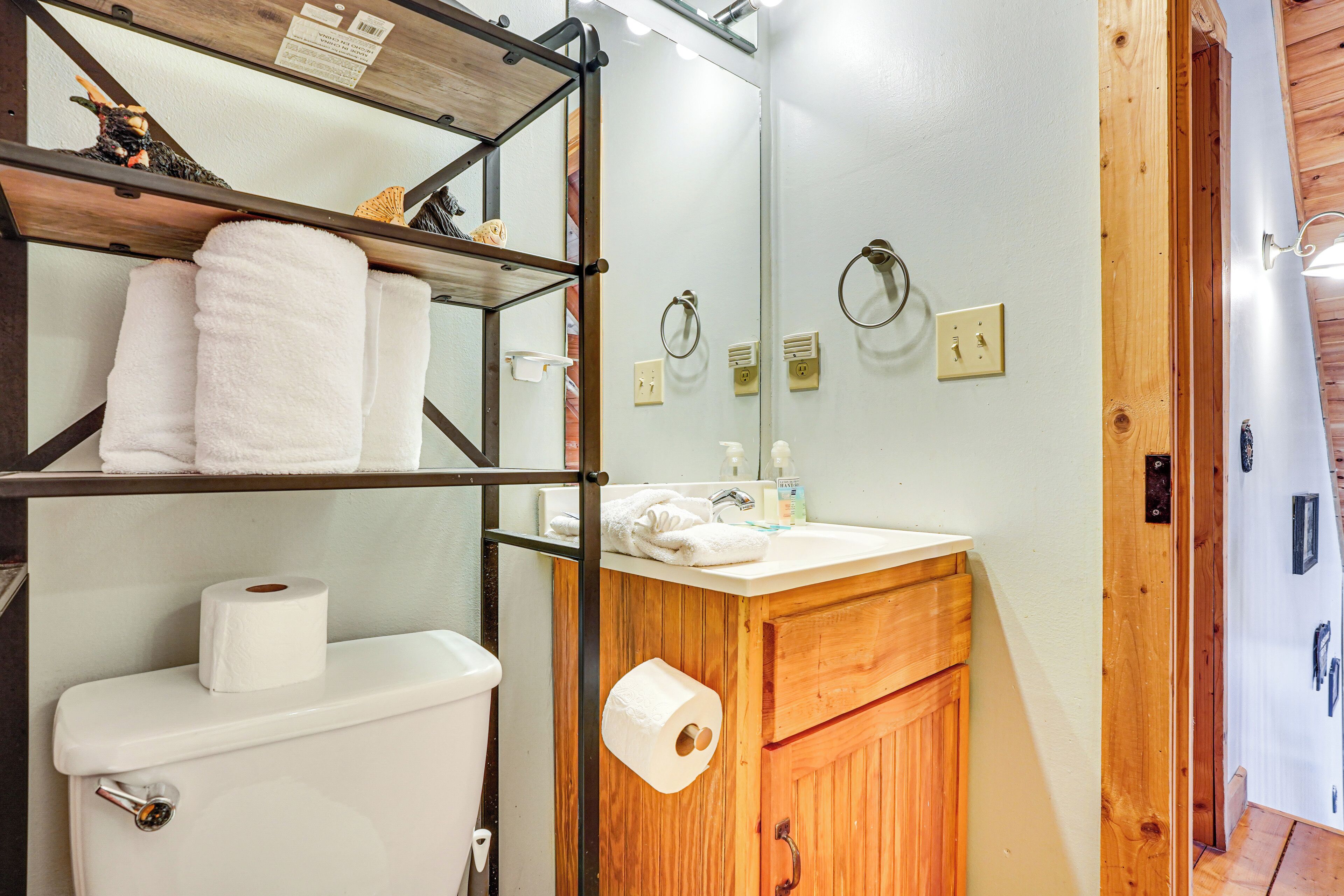 Een badkamer met een houten wastafelmeubel, een toilet met een rol toiletpapier, een plank met handdoeken en een spiegel.