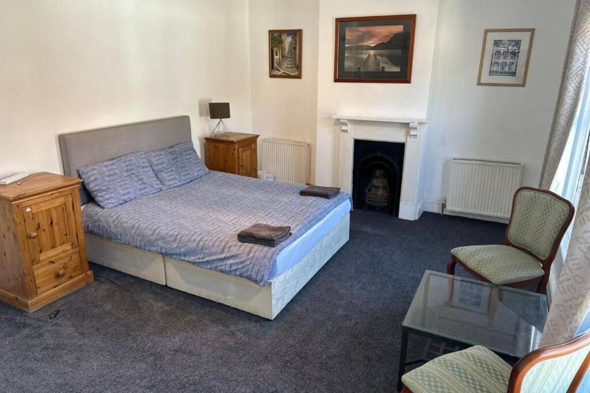 Quarto com cama, poltrona, mesinha, lareira e quadros na parede.