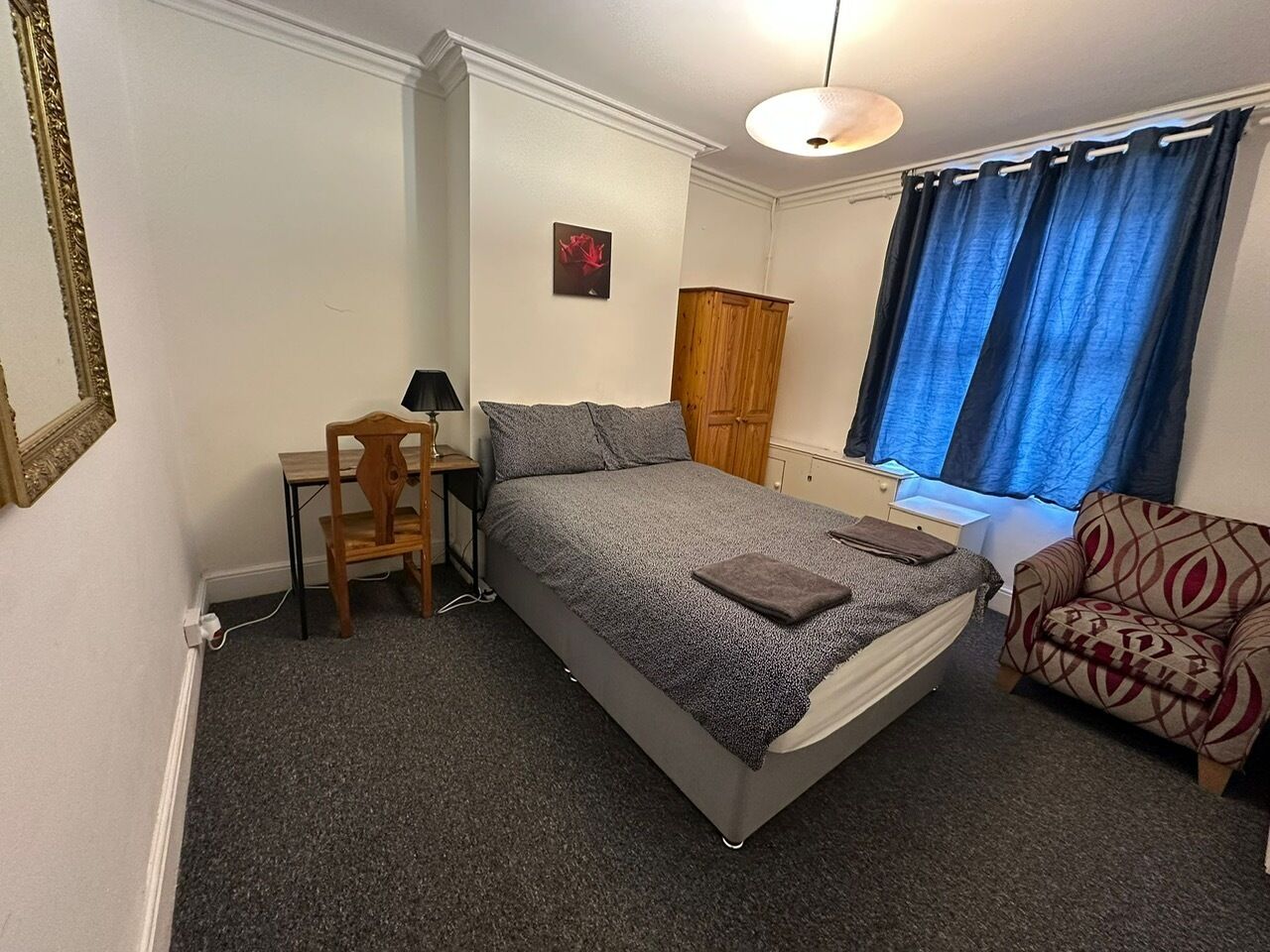 A bedroom with a bed, a desk, a chair, a wardrobe, and a window with curtains.
