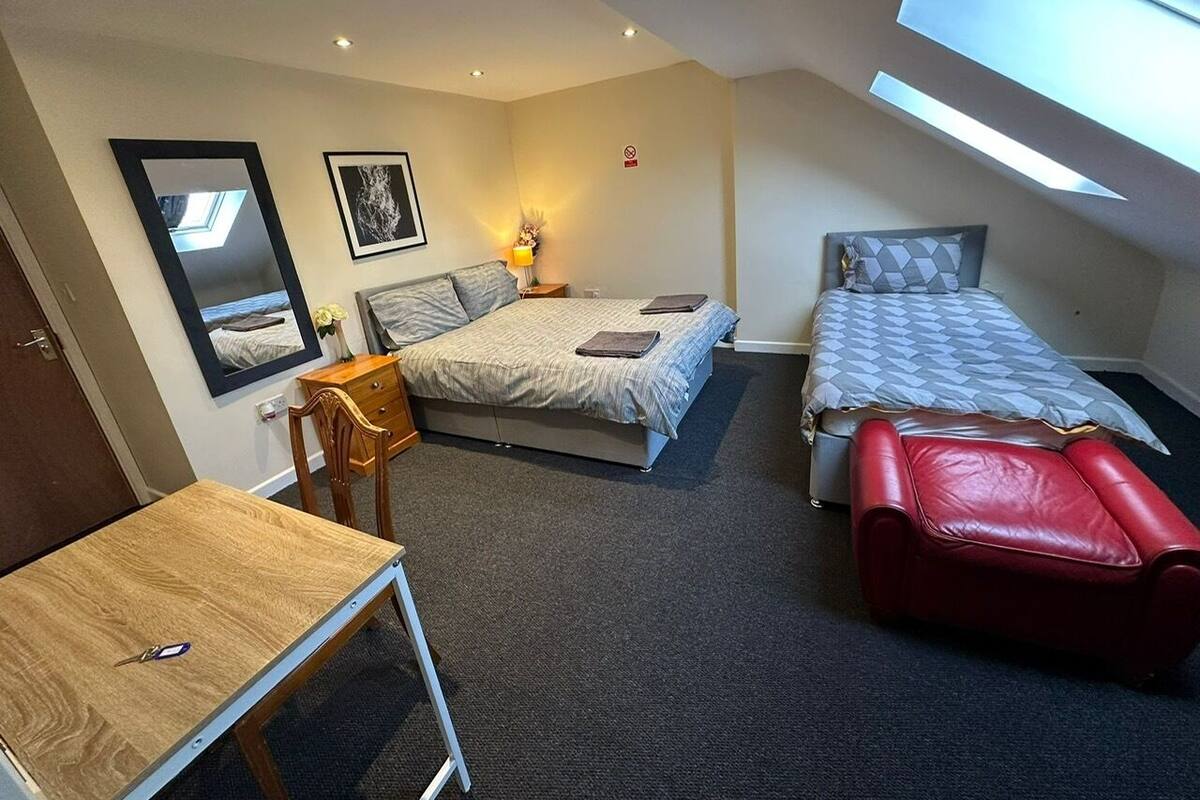Quarto de hotel compacto com cama, escrivaninha, cadeira e um pequeno espaço para sentar.