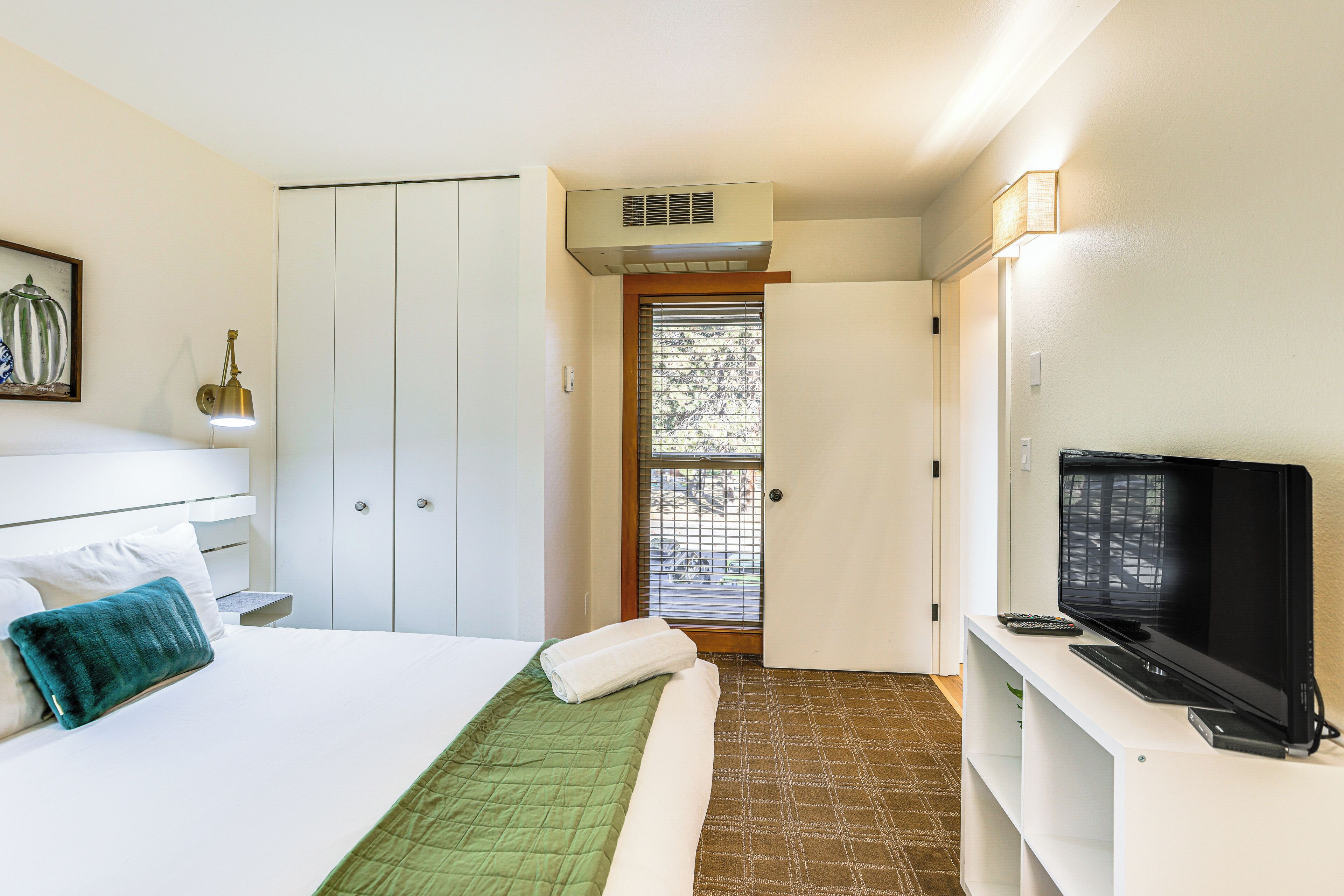 Quarto de hotel com cama, televisão, guarda-roupa e janela com cortinas.