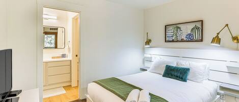 Ett hotellrum med en säng, en tv, ett skrivbord och ett badrum som syns genom en öppen dörr.