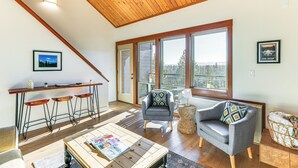 Un espacio habitable amplio con techo de madera, ventanas grandes, una barra con taburetes y una zona de estar acogedora.
