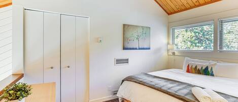 A bedroom with a bed, a bedside table with a plant, a painting on the wall, and a window with blinds.