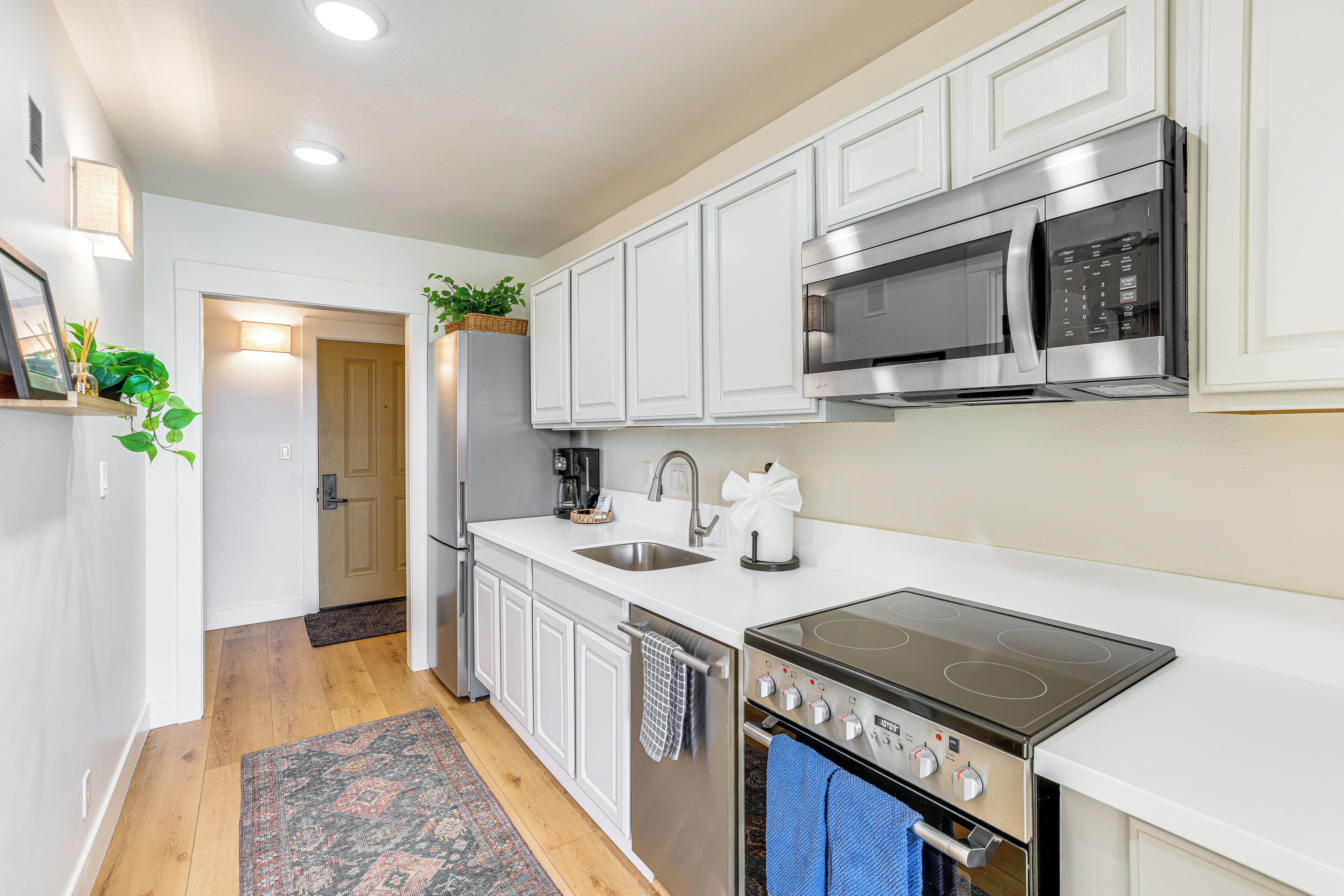A modern kitchen with white cabinets, stainless steel appliances, and a wooden floor.