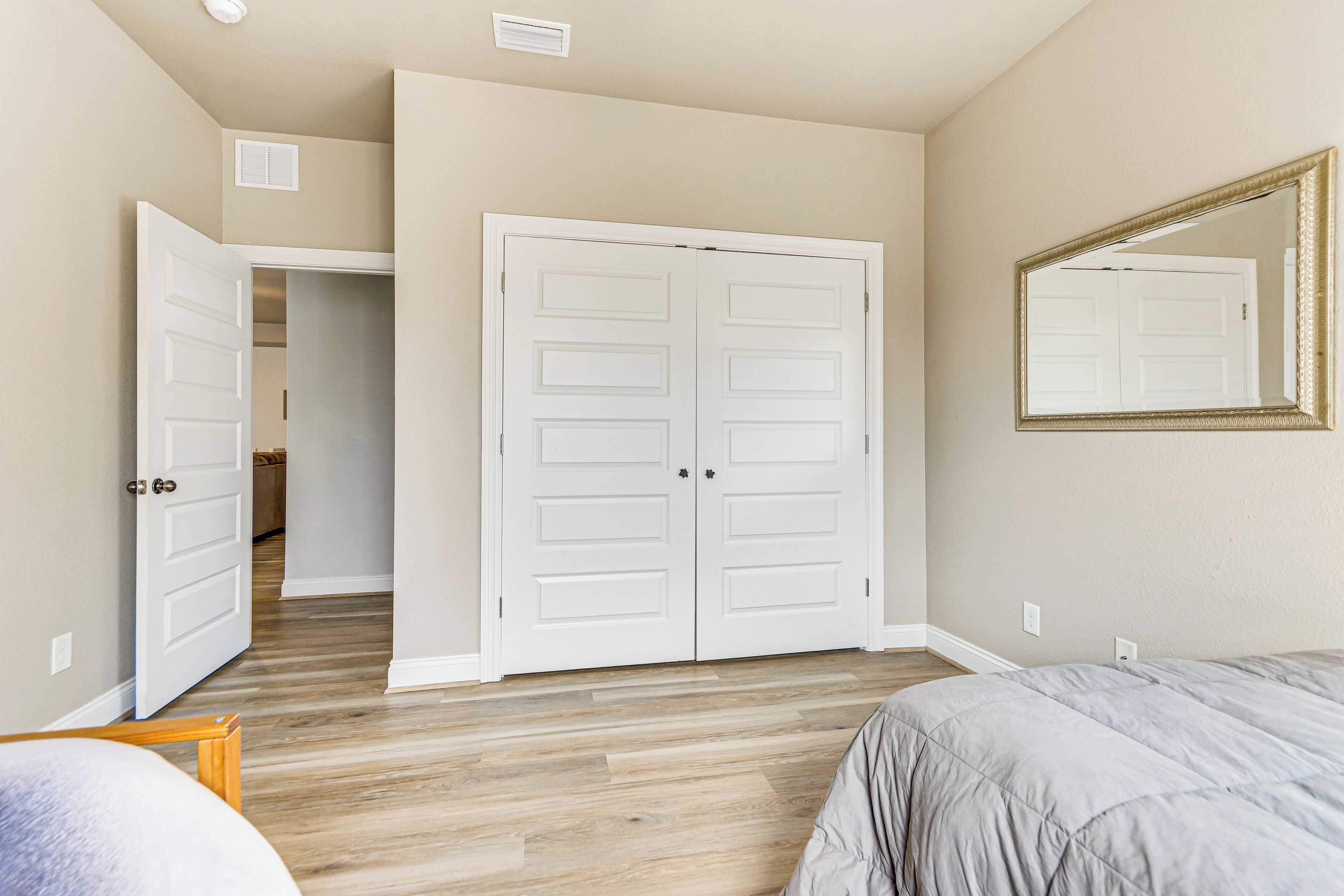 A bedroom with a wooden floor, a double door, a bed, and a mirror.