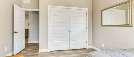 A bedroom with a wooden floor, a double door, a bed, and a mirror.