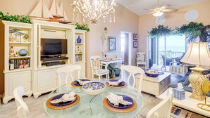 A dining area with a glass table, white chairs, and a chandelier. - Community Pool: Coastal Escape in Flagler Beach (Flagler Beach)