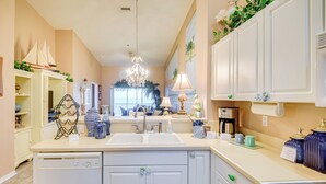 A kitchen with white cabinets, a dishwasher, a sink, and a countertop with various items. - Community Pool: Coastal Escape in Flagler Beach (Flagler Beach)