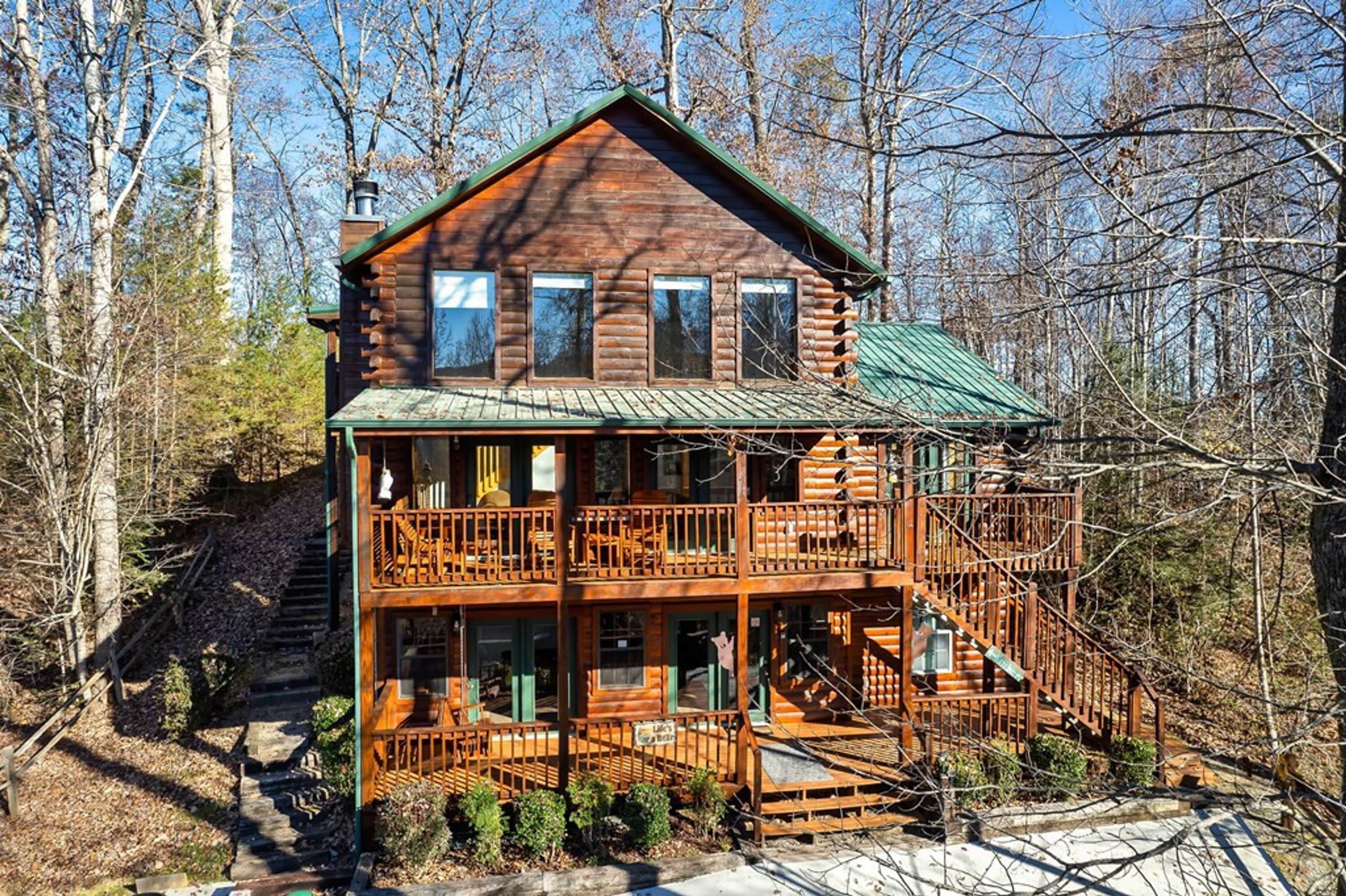 A log cabin with a green roof, multiple balconies, and a staircase leading to the upper level.