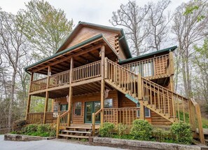 A two-story log cabin with a balcony, a staircase, and a porch. - Stunning Cabin w Hot Tub Pool Table Arcades (Sevierville)